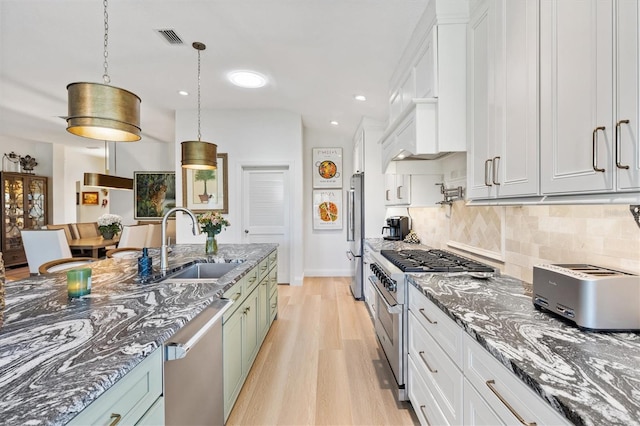 kitchen with decorative backsplash, dark stone countertops, stainless steel appliances, light wood-style floors, and a sink