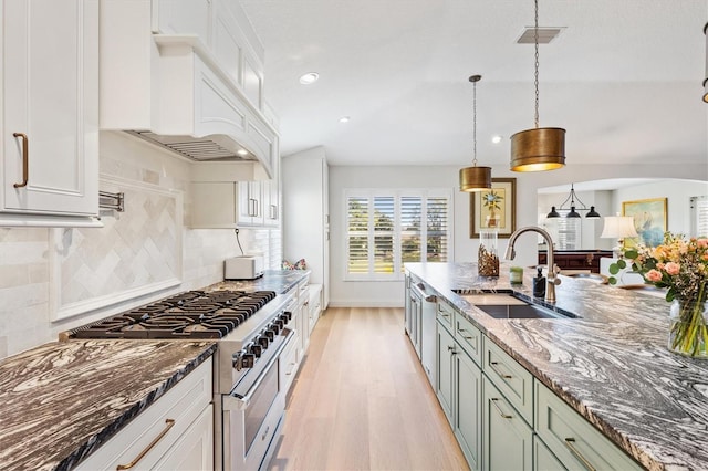 kitchen featuring custom range hood, high end stainless steel range oven, light wood-style flooring, white cabinetry, and a sink