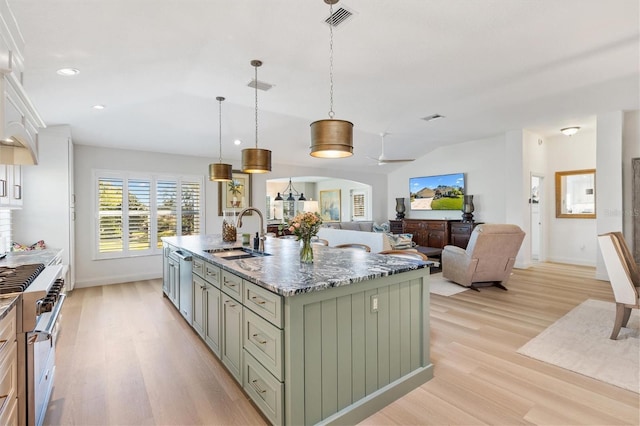 kitchen featuring light wood finished floors, visible vents, appliances with stainless steel finishes, a sink, and dark stone countertops