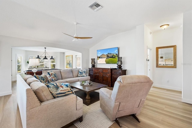 living area featuring vaulted ceiling, light wood-style flooring, arched walkways, and visible vents