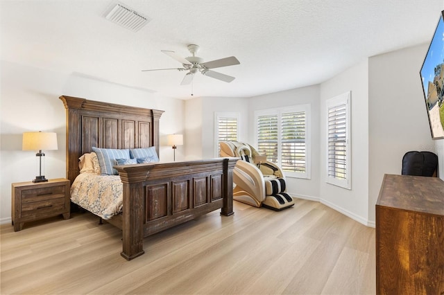 bedroom with a textured ceiling, a ceiling fan, baseboards, visible vents, and light wood-style floors