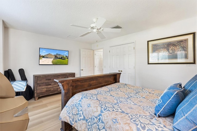 bedroom featuring light wood finished floors, ceiling fan, visible vents, and a textured ceiling