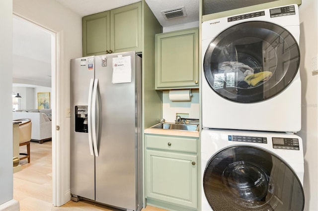 washroom featuring light wood-type flooring, stacked washer and clothes dryer, visible vents, and a sink