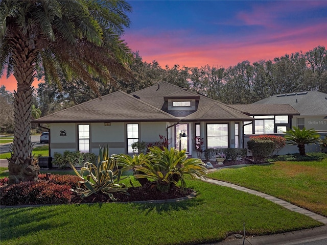 view of front facade with a shingled roof, a front yard, and stucco siding