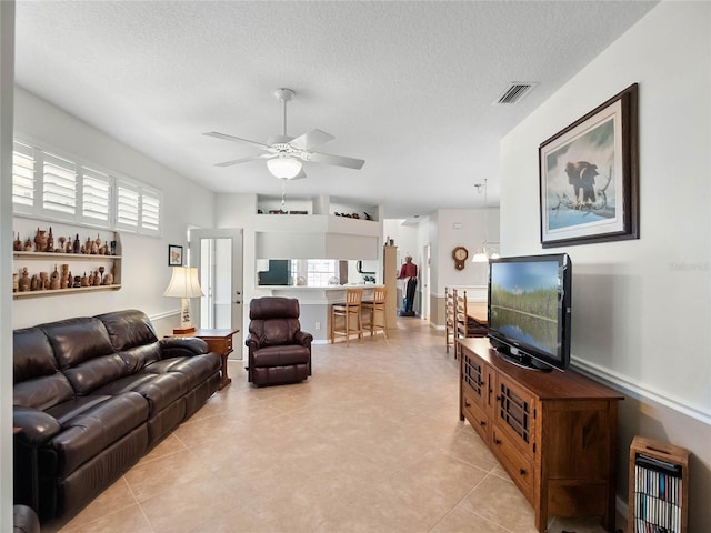 living area featuring a wealth of natural light, visible vents, ceiling fan, and a textured ceiling