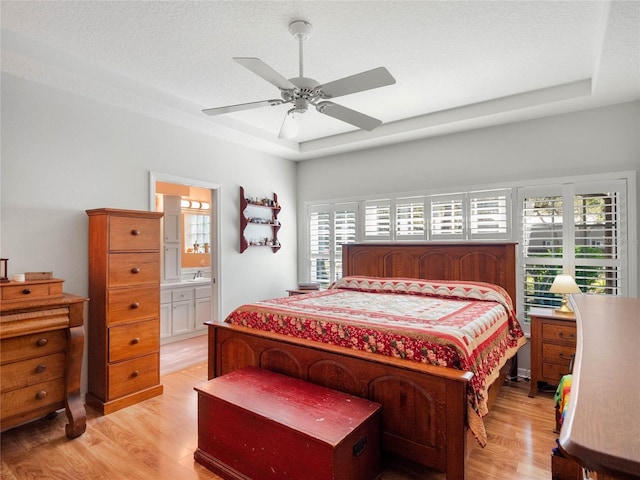 bedroom featuring a textured ceiling, light wood-type flooring, and a raised ceiling