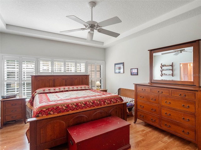 bedroom with light wood-style floors, multiple windows, a tray ceiling, and a textured ceiling