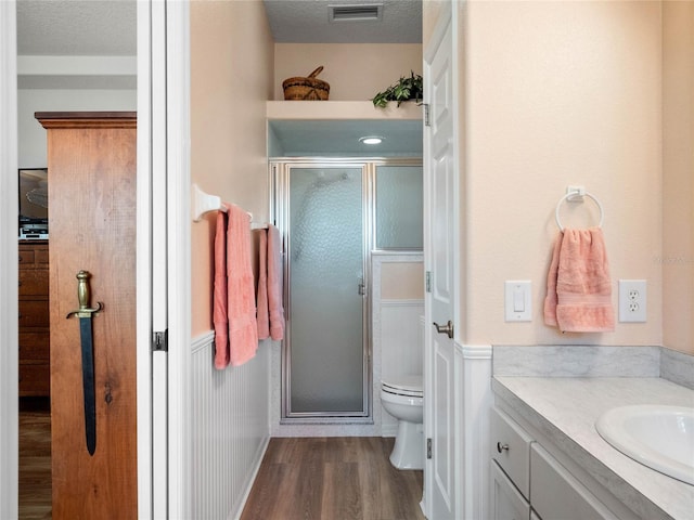 bathroom with visible vents, toilet, a stall shower, vanity, and wood finished floors