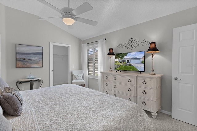 bedroom featuring a textured ceiling, baseboards, a spacious closet, lofted ceiling, and ceiling fan