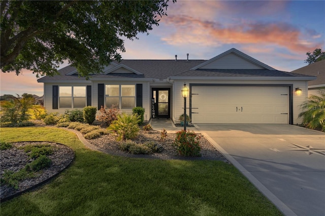 ranch-style house featuring roof with shingles, an attached garage, concrete driveway, and a lawn