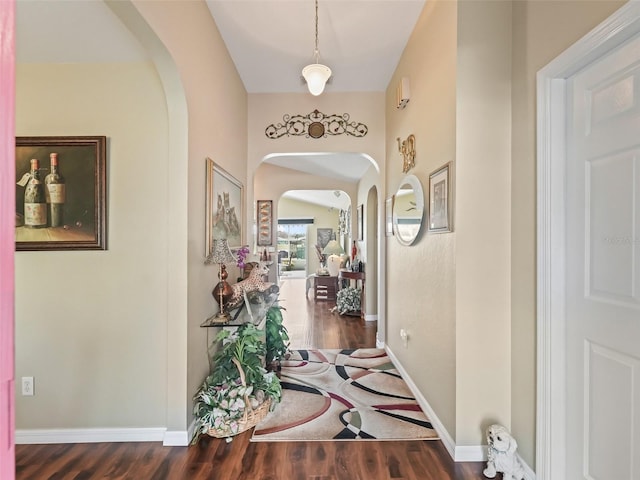 hallway featuring arched walkways, baseboards, and wood finished floors