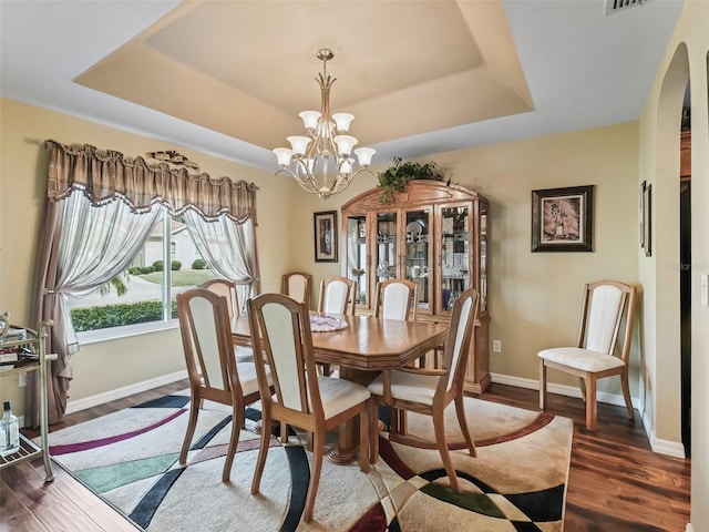 dining area with arched walkways, baseboards, a tray ceiling, dark wood finished floors, and an inviting chandelier