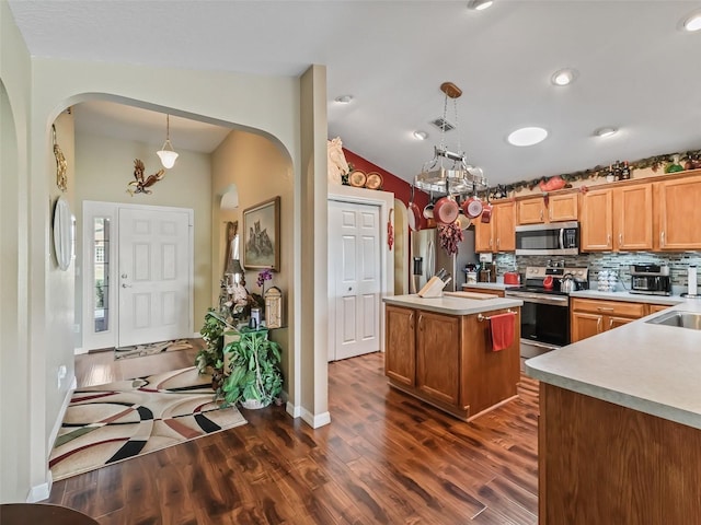 kitchen with arched walkways, stainless steel appliances, vaulted ceiling, and a center island