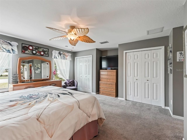 carpeted bedroom with two closets, visible vents, a ceiling fan, a textured ceiling, and baseboards