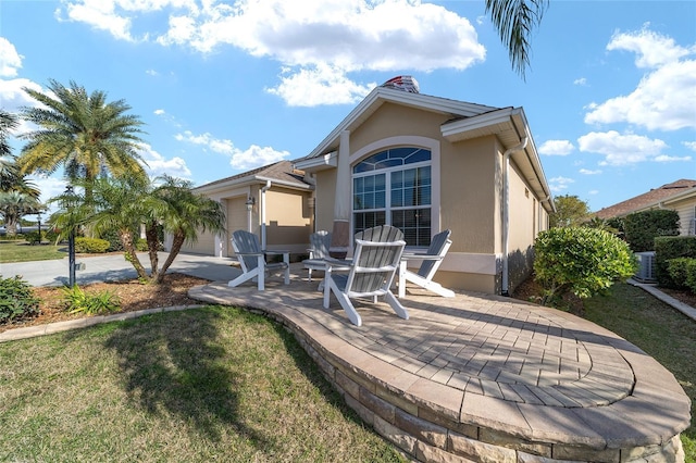 back of property featuring a garage, a yard, a patio area, central AC, and stucco siding