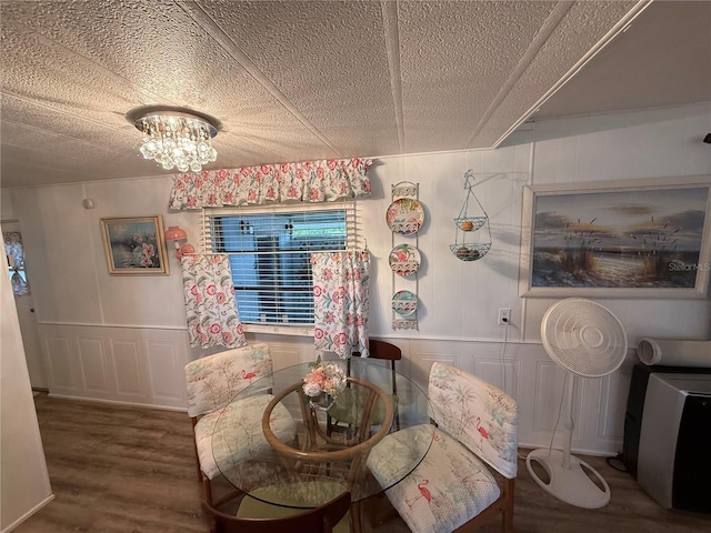 dining room featuring a notable chandelier, a textured ceiling, wood finished floors, and a decorative wall