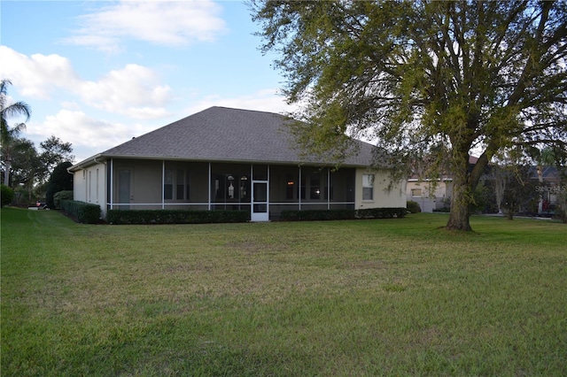 rear view of property featuring stucco siding, a yard, a sunroom, and a shingled roof