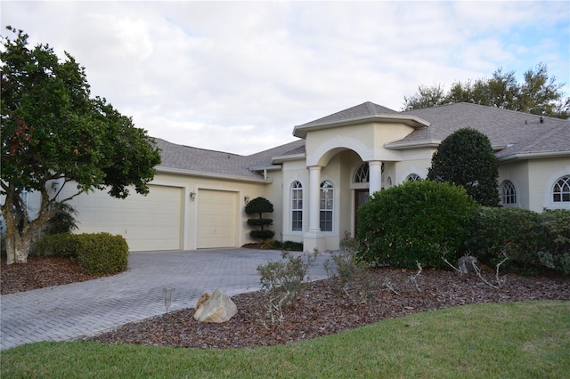 view of front of home with decorative driveway, a shingled roof, an attached garage, and stucco siding