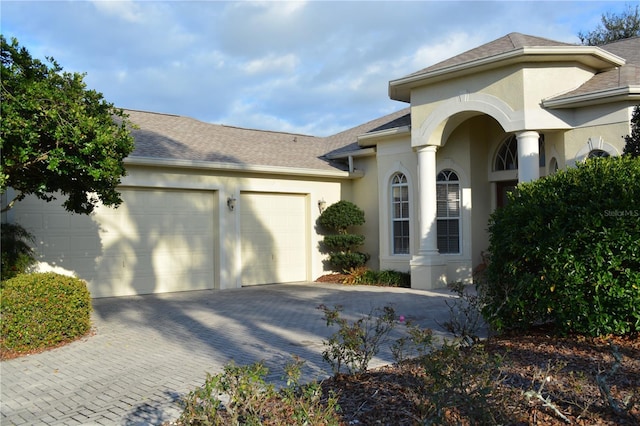 view of front facade with stucco siding, decorative driveway, a garage, and roof with shingles