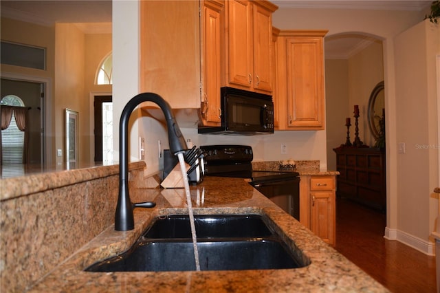 kitchen with black appliances, ornamental molding, a sink, wood finished floors, and light stone countertops