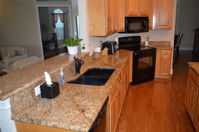 kitchen featuring wood finished floors, light stone countertops, black appliances, and a sink