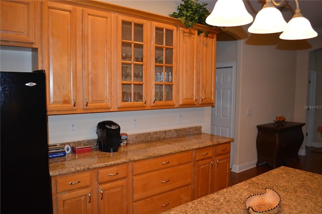 kitchen featuring light stone counters, glass insert cabinets, brown cabinetry, and freestanding refrigerator
