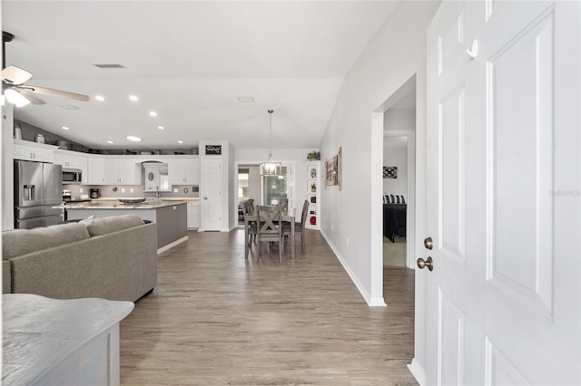 living area featuring vaulted ceiling, ceiling fan with notable chandelier, visible vents, and light wood-style floors