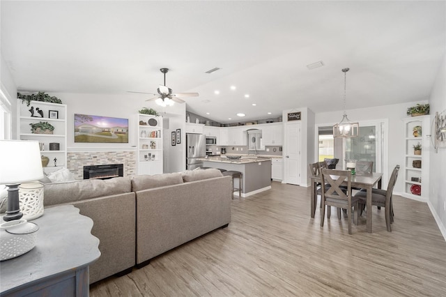 living area featuring lofted ceiling, ceiling fan, a warm lit fireplace, recessed lighting, and light wood-style floors