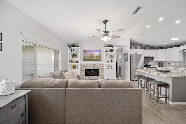 living room featuring visible vents, a ceiling fan, lofted ceiling, light wood-type flooring, and a fireplace