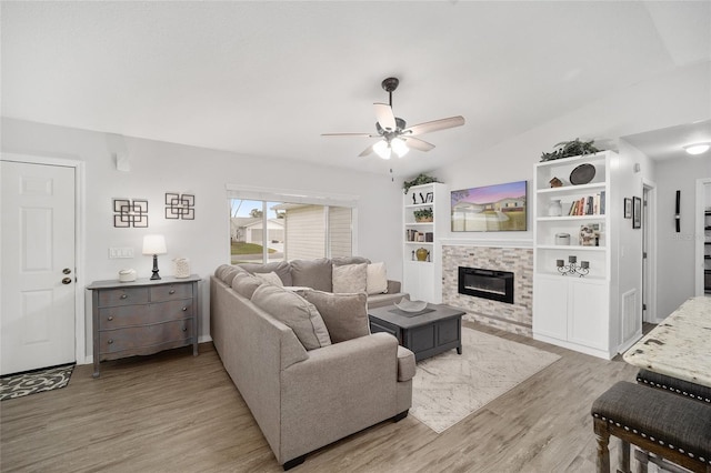 living area with lofted ceiling, ceiling fan, a tile fireplace, and light wood-style flooring