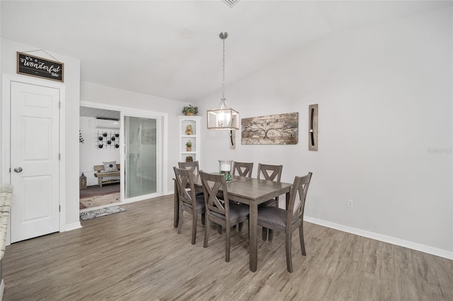 dining room featuring lofted ceiling, a wall unit AC, baseboards, and wood finished floors