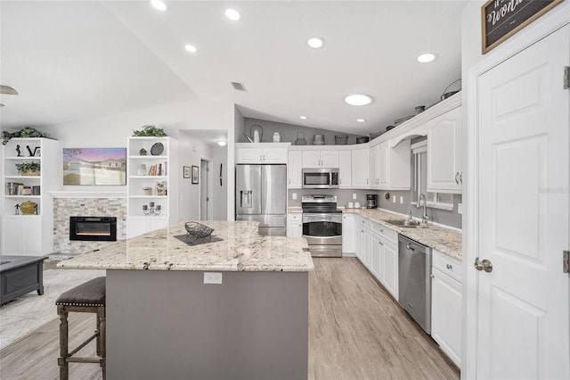 kitchen featuring lofted ceiling, stainless steel appliances, a sink, white cabinets, and a center island