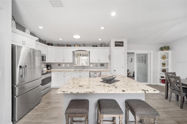 kitchen featuring visible vents, a breakfast bar area, appliances with stainless steel finishes, white cabinetry, and a sink