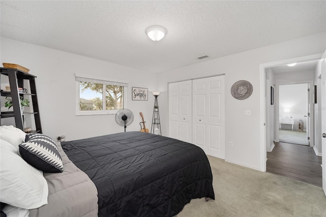 bedroom featuring light carpet, visible vents, baseboards, a textured ceiling, and a closet