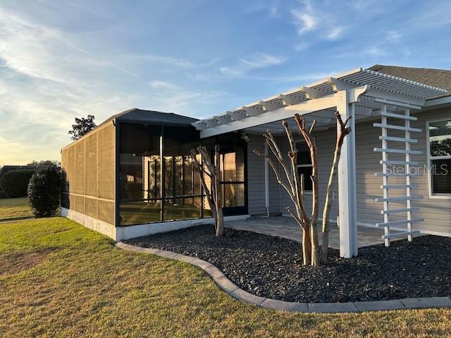 back of property featuring a sunroom, a patio area, a lawn, and a pergola