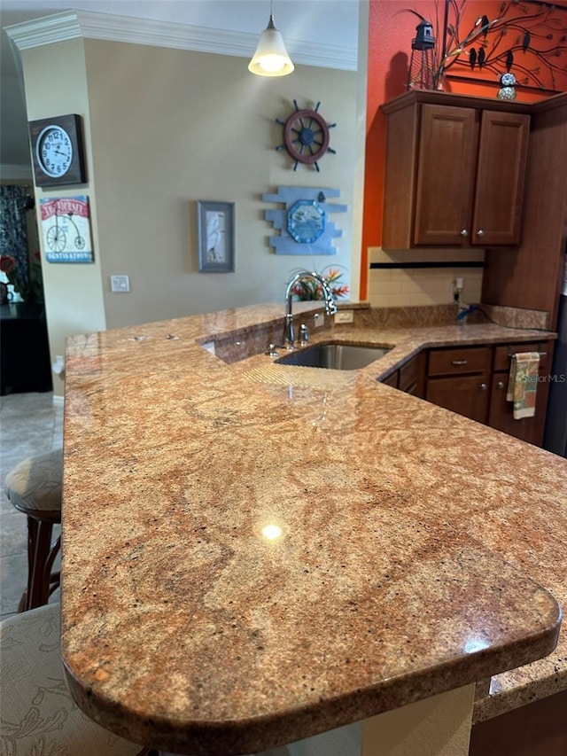 kitchen featuring light stone counters, crown molding, a peninsula, a sink, and pendant lighting