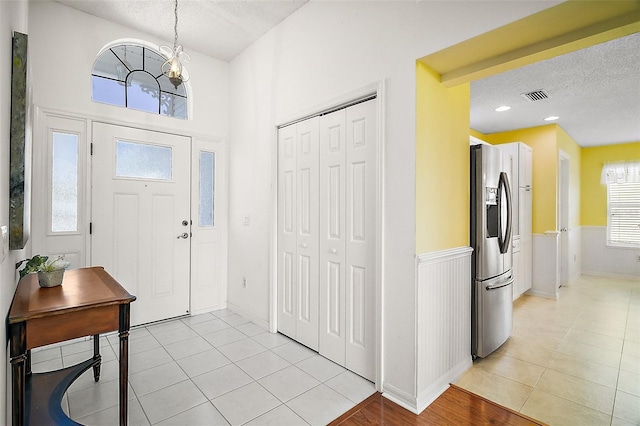 entrance foyer with a wainscoted wall, visible vents, a textured ceiling, and light tile patterned flooring