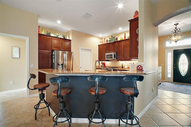 kitchen featuring light stone counters, a breakfast bar area, stainless steel appliances, visible vents, and a peninsula