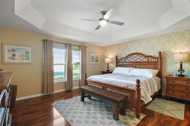 bedroom with ceiling fan, wood finished floors, baseboards, a tray ceiling, and wallpapered walls