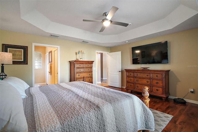 bedroom featuring wood finished floors, a ceiling fan, visible vents, baseboards, and a tray ceiling