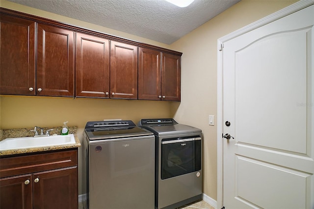 clothes washing area featuring cabinet space, a sink, a textured ceiling, washer and dryer, and baseboards