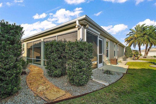 view of side of property with a sunroom, a yard, and stucco siding