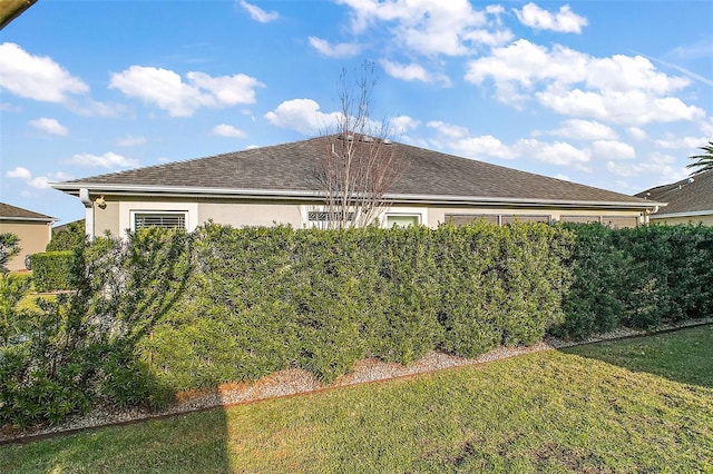 view of side of home with a shingled roof, a lawn, and stucco siding