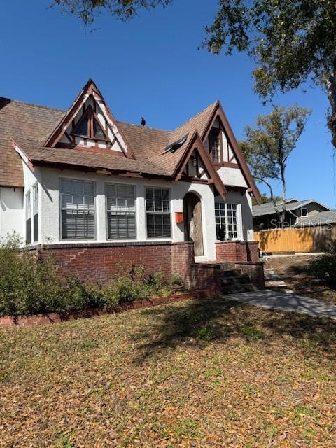 tudor-style house featuring brick siding, fence, and a front lawn