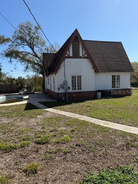 view of side of property with roof with shingles, brick siding, stucco siding, a lawn, and central AC unit