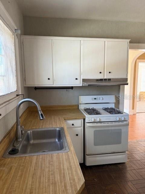 kitchen featuring arched walkways, under cabinet range hood, a sink, white cabinetry, and white gas range