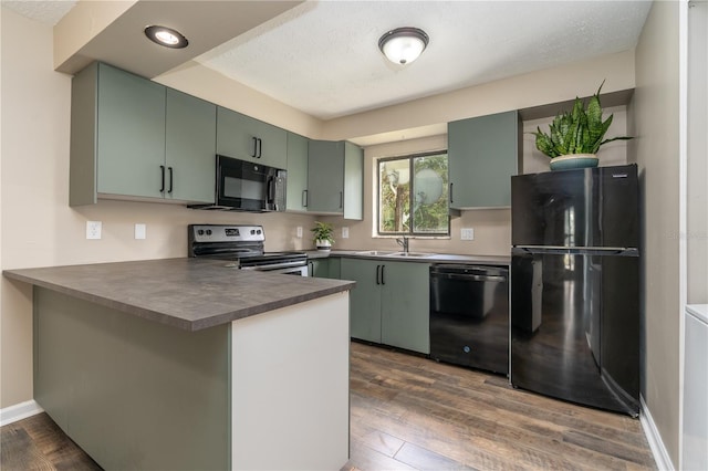 kitchen featuring dark wood-style floors, dark countertops, a sink, a peninsula, and black appliances