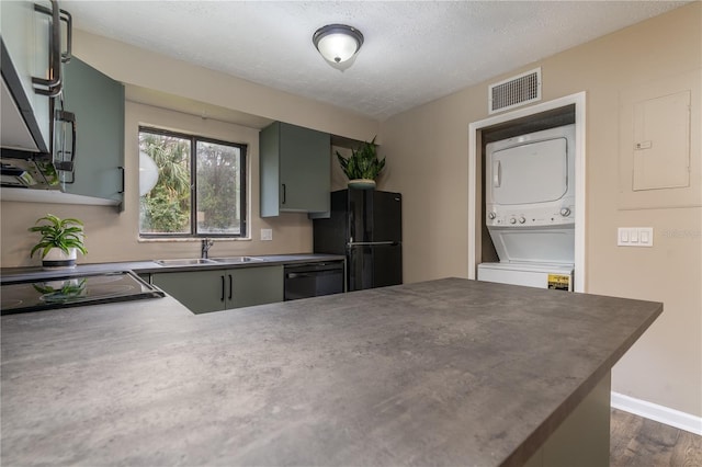 kitchen featuring stacked washer / drying machine, visible vents, a sink, a peninsula, and black appliances