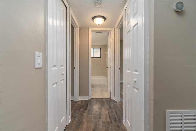 corridor with visible vents, dark wood-type flooring, and a textured ceiling