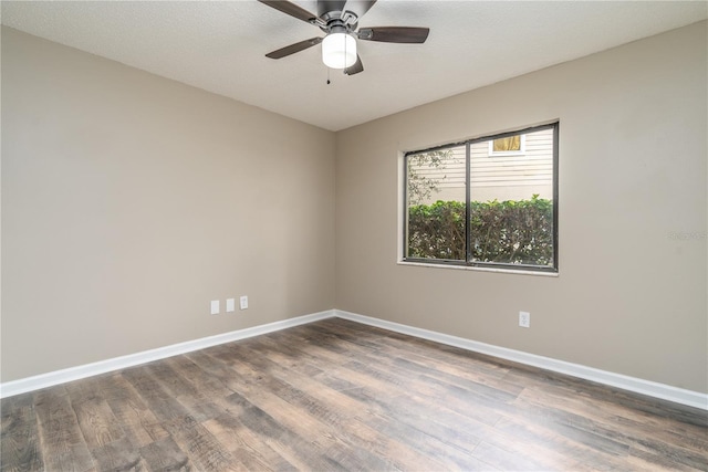 empty room with a ceiling fan, dark wood finished floors, and baseboards